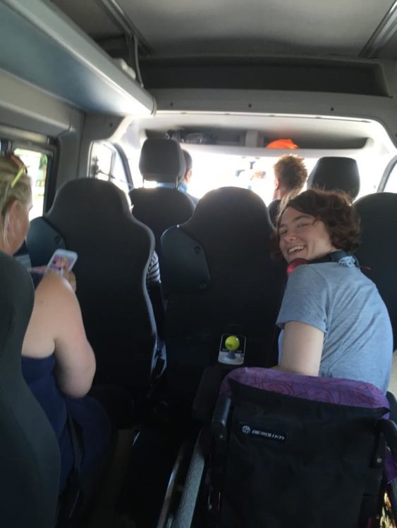 Liesl Hammer smiling from her wheelchair inside an accessible minibus while travelling with friends.