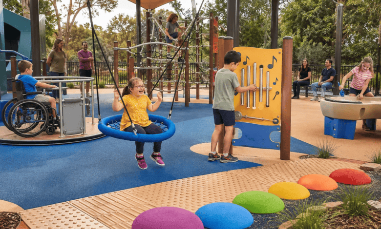Children play in an inclusive sensory playground with a basket swing, accessible roundabout, musical play panel, rope climber, water play area and textured pathways while parents watch nearby.