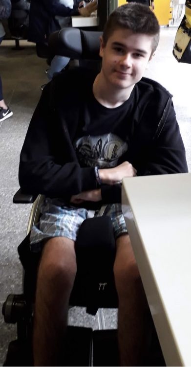 Liam as a teenager, seated in a wheelchair at a table and looking towards the camera.