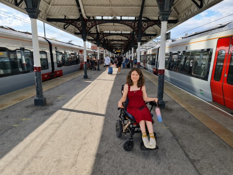 Wheelchair user in a red dress on a train platform, with trains on either side.