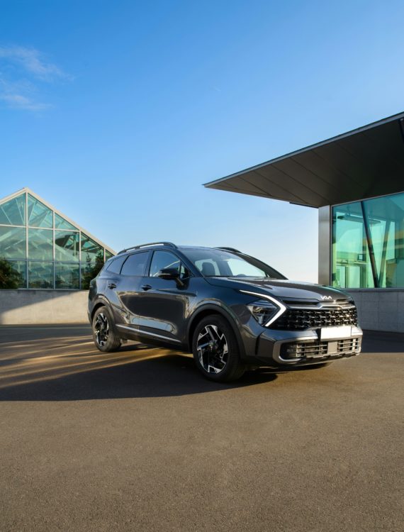 Grey Kia Sportage parked outside a modern glass building, viewed from the front and side.