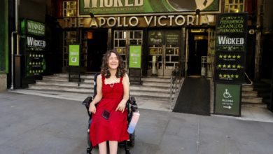Wheelchair user in a red dress outside the Apollo Victoria Theatre, with Wicked signage and an accessible ramp.