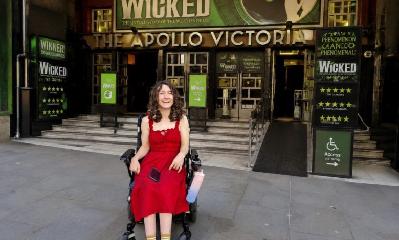 Wheelchair user in a red dress outside the Apollo Victoria Theatre, with Wicked signage and an accessible ramp.