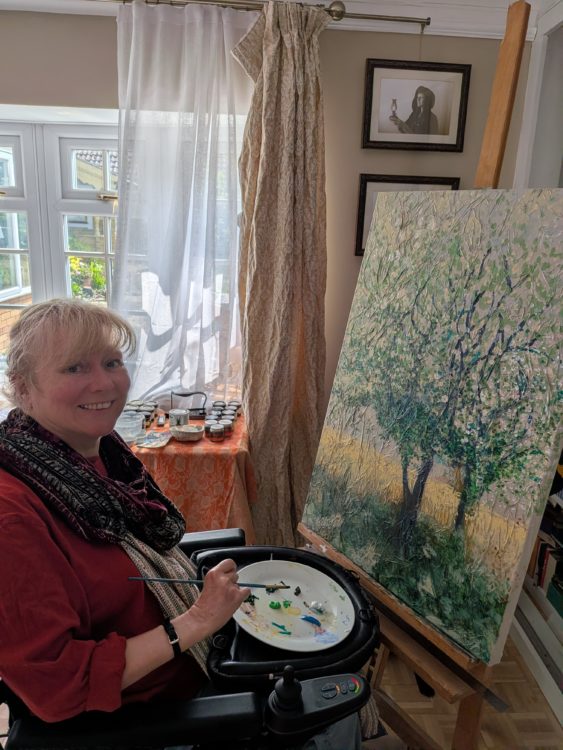Clare, who has an incomplete spinal cord injury, painting at an easel with a Trabasack supporting her palette.
