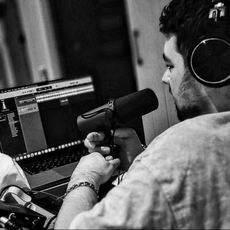 JOHKES wearing headphones speaks into a microphone while using audio-editing software on a laptop.