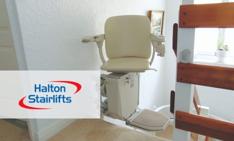 Cream-coloured stairlift with a fold-down footrest installed at the top of a staircase, beside a wooden banister.